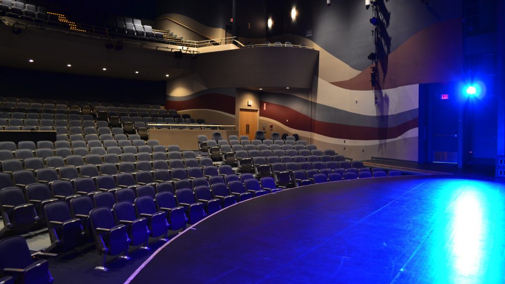 Salle de spectacle vide vue du côté jardin de la scène, sous un éclairage bleu.