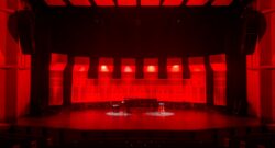 Photo of an empty theatre with a grand piano in the middle of the stage, lit up in red