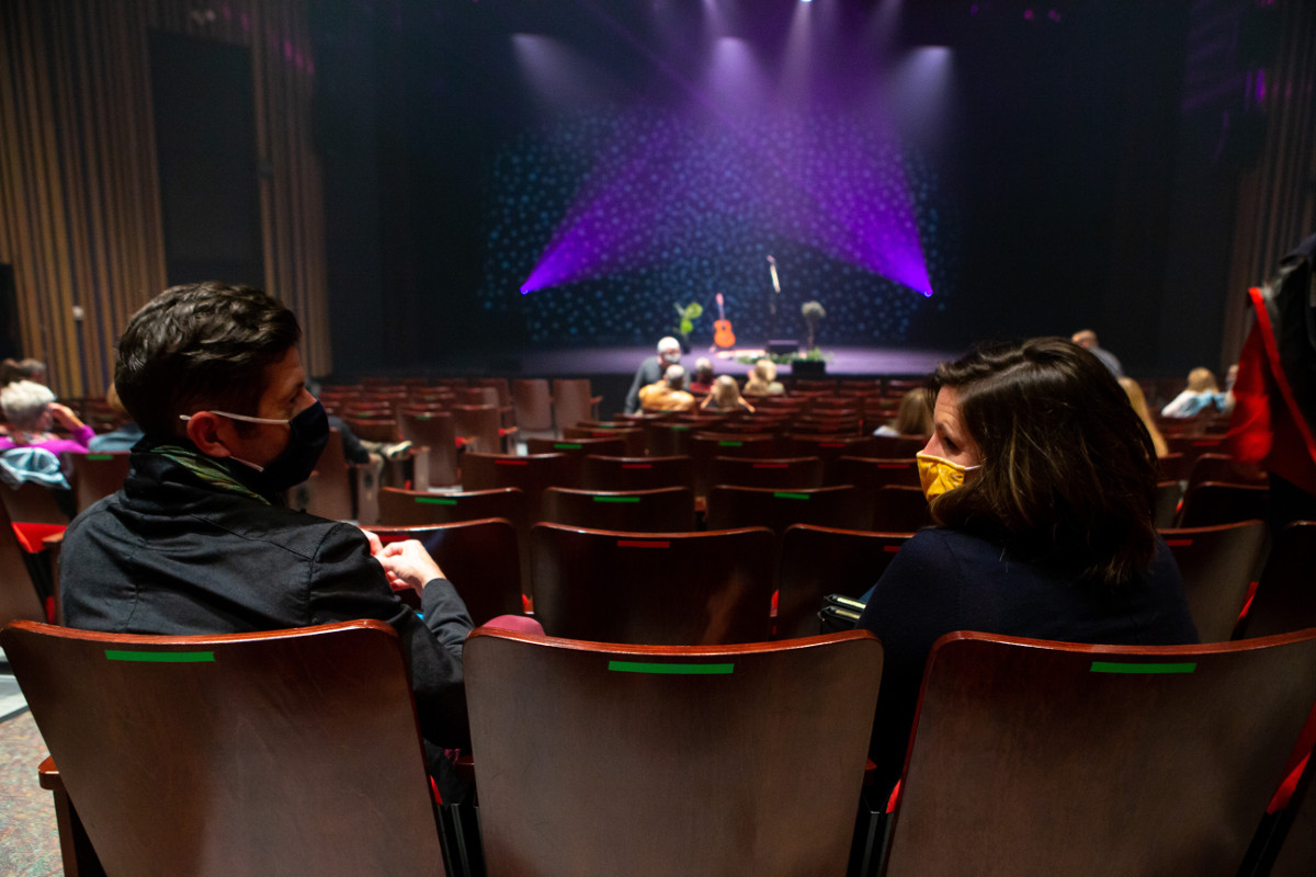 Les spectateurs portant des masques attendent le début d'un spectacle dans une salle presque vide en raison des règles de distanciation physique.