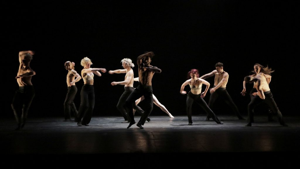 Modern dancers in black pants and bare chest on stage performing.