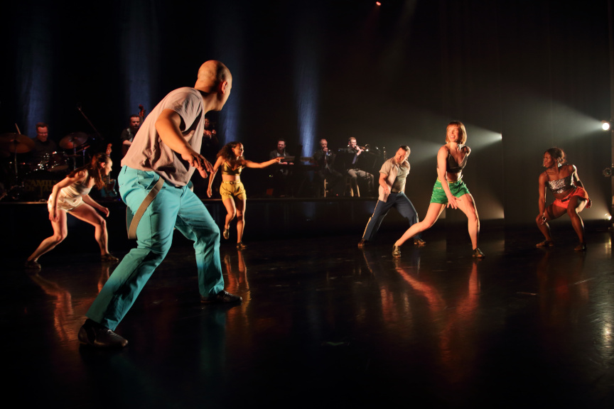 Dancers performing with a live orchestra in the background.