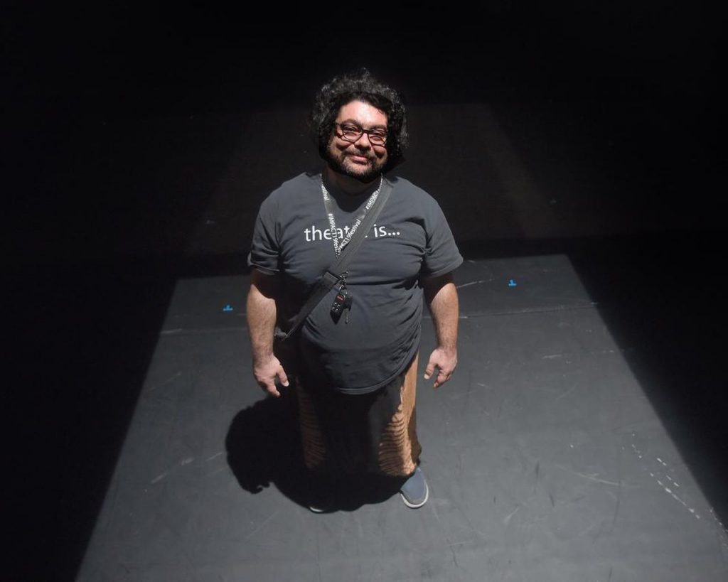 Majdi Bou-Matar stands in the spotlight of a black box theatre