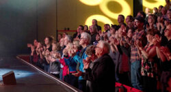 Audience members are standing in their seats, smiling and clapping, while enjoying a performance at Le Pôle culturel de Chambly.