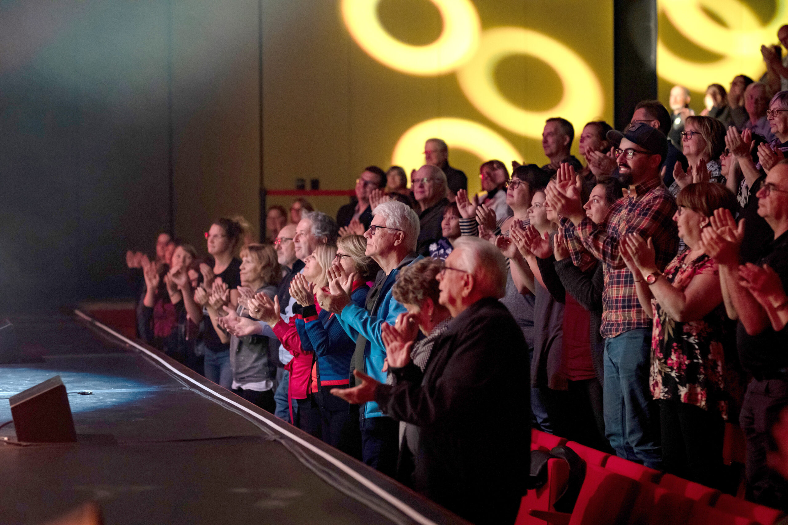 Audience members are standing in their seats, smiling and clapping, while enjoying a performance at Le Pôle culturel de Chambly.