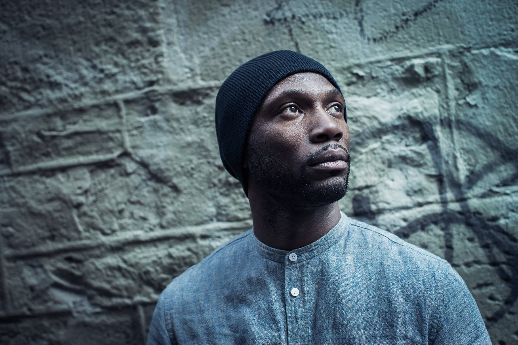 Crazy Smooth debout devant un mur de pierre, regardant au loin.