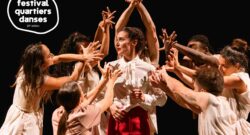 Des danseur(euse)s sur scène, vêtus de blanc, les mains en l'air, les doigts écartés. Ils (Elles) tournent autour d'une danseuse qui a un regard inquiet.