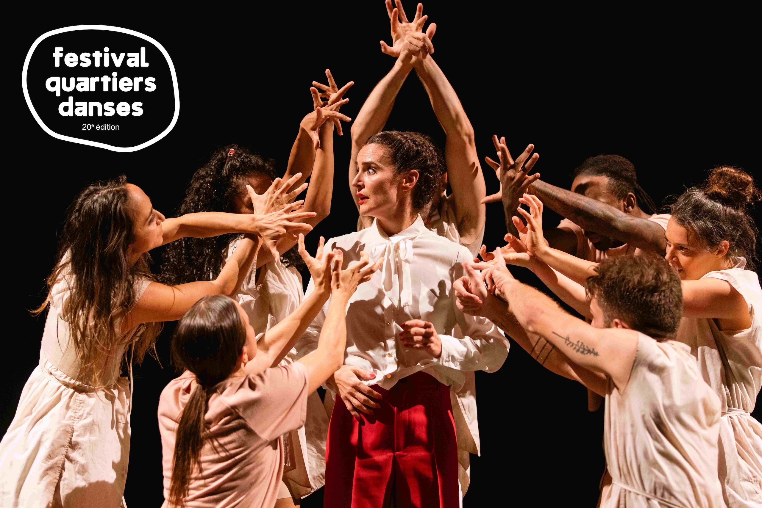 Dancers on stage wearing white, hands in the air with their fingers spread. They are circling around one dancer who has a concerned look on her face.