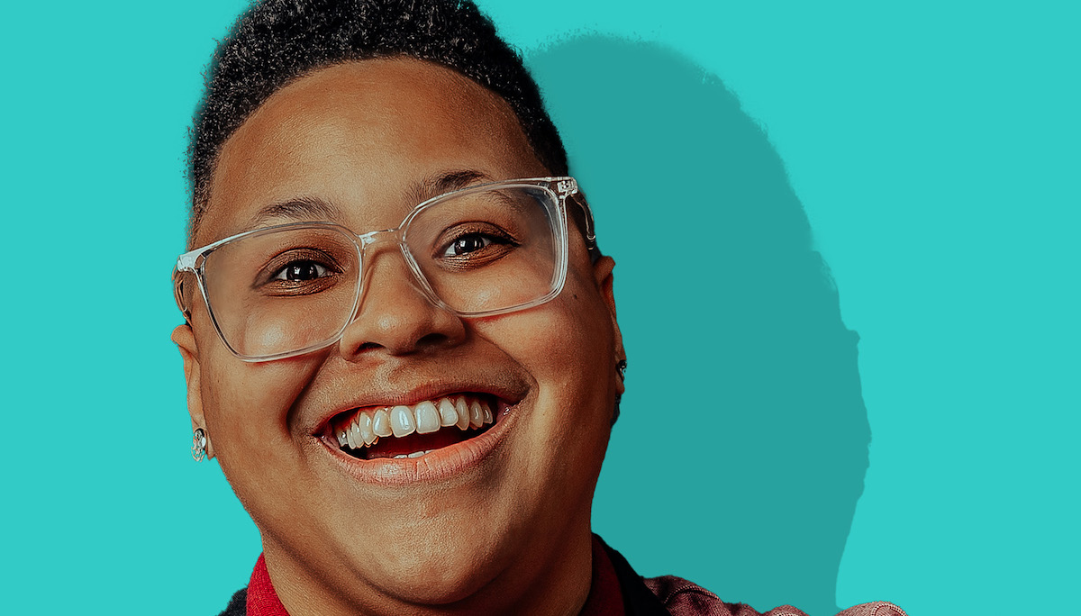 Evelyn is standing in front of a bright teal background, smiling towards the camera.