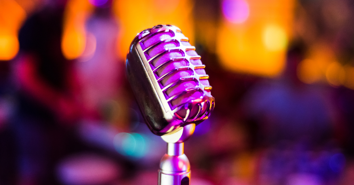 Un microphone de style rétro se trouve au centre de l'image. L'arrière-plan orange et rose est flou.