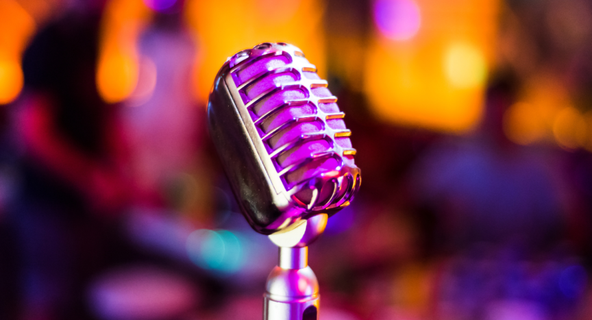 A retro-style microphone is in the centre of the image. The orange and pink-hued background is blurred.