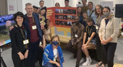 Members of the Canadian delegation at tanzmesse 2022. Some folks are standing, some sitting, and some kneeling around the "Danse + Canada + Dance" booth in the Agora.