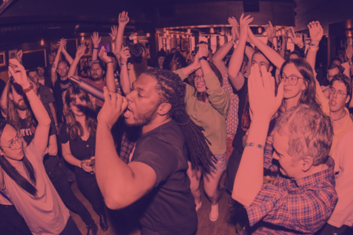 A crowd of audience members with their hands in the air during a performance.