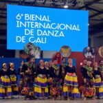 Image d'un groupe de danse folklorique à Cali, en Colombie, debout devant une bannière portant l'inscription « 6e Bienal Internacional de Danza de Cali ».