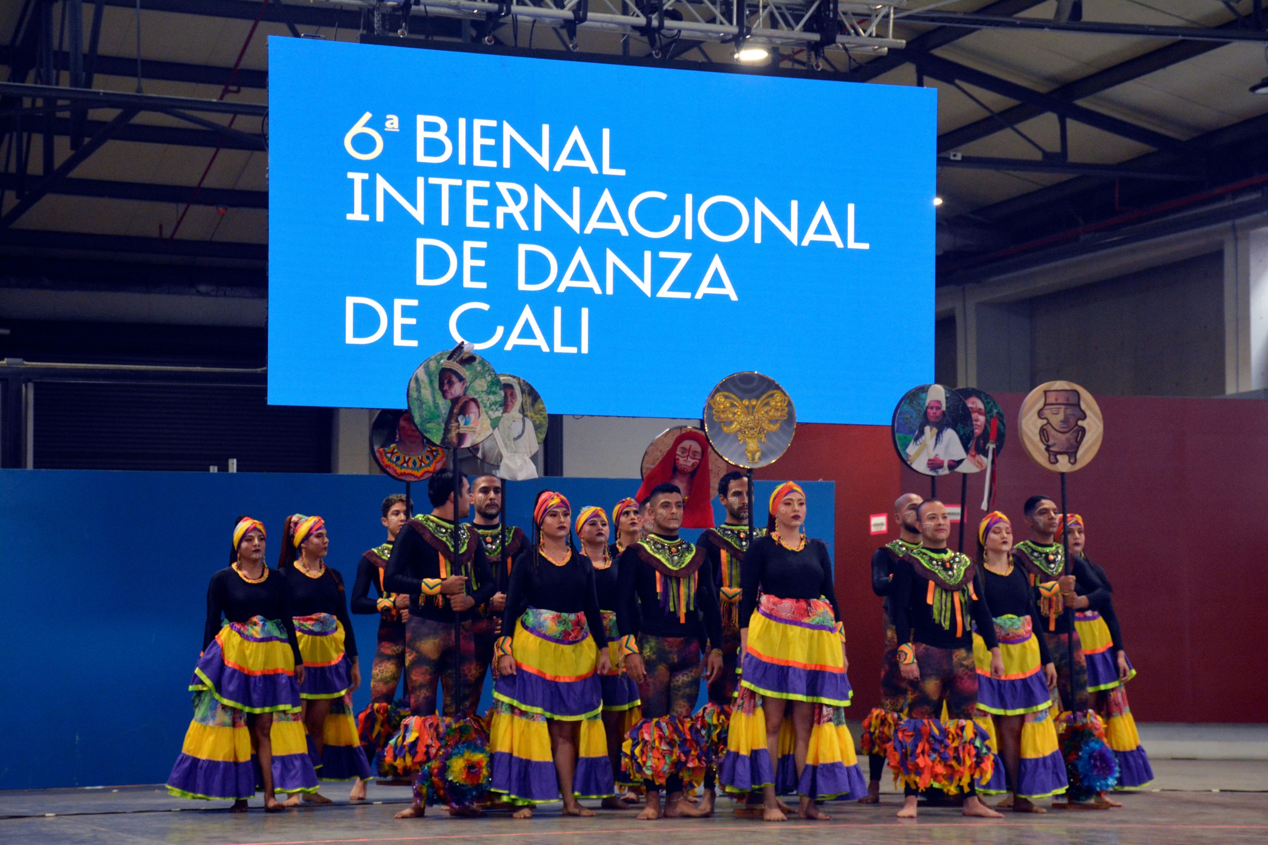 Image d'un groupe de danse folklorique à Cali, en Colombie, debout devant une bannière portant l'inscription « 6e Bienal Internacional de Danza de Cali ».