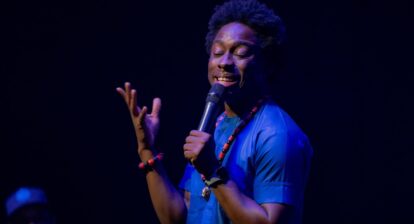 Un chanteur tient un micro et fait des gestes vers le haut de la scène.