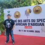 A person stands in front of a large sign that reads marché des arts du spectacle africain