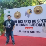 A person stands in front of a large sign that reads marché des arts du spectacle africain