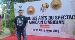 A person stands in front of a large sign that reads marché des arts du spectacle africain