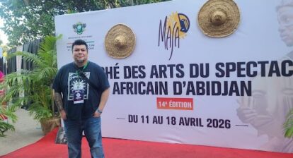 A person stands in front of a large sign that reads marché des arts du spectacle africain