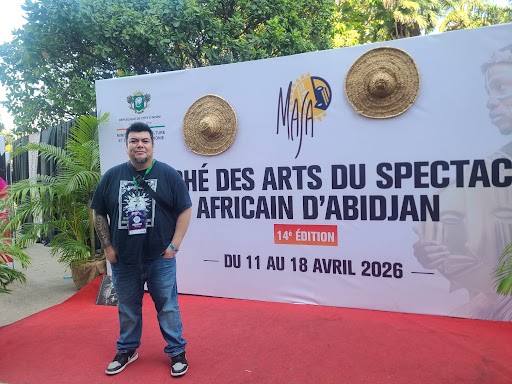 A person stands in front of a large sign that reads marché des arts du spectacle africain