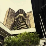 Au cœur commercial d’Abidjan (dans le quartier du Plateau), un animateur annonce le prochain événement de la MASA dans la cour de l’Institut Français de Côte d’Ivoire, un exemple emblématique du brutalisme tropical post-indépendance. Les pare-soleil en béton brut apparent et les volumes géométriques audacieux étaient caractéristiques de l’architecture publique ouest-africaine des années 1970.