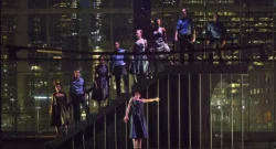 A group of dancers standing on a staircase on a dark stage.