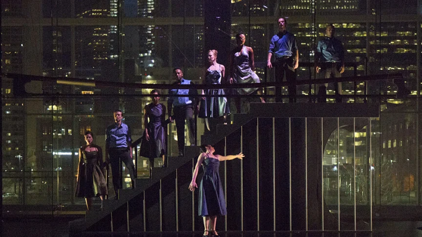 A group of dancers standing on a staircase on a dark stage.