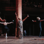 Femme chantant avec les bras dans les airs, entourée de quatre danseurs.