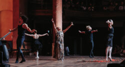Femme chantant avec les bras dans les airs, entourée de quatre danseurs.